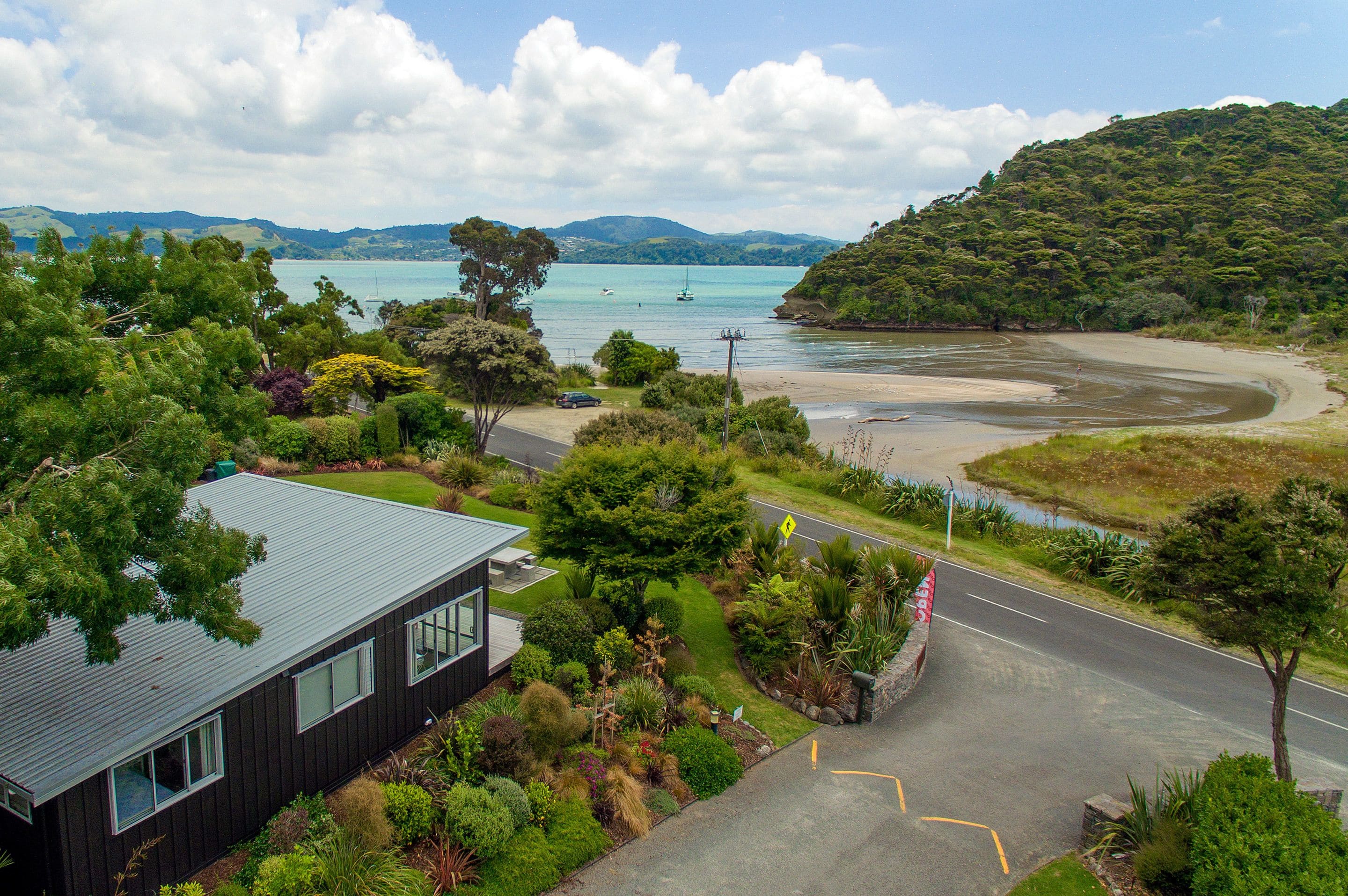 A coastal property with a road leading to a beach, surrounded by lush greenery and a view of the sea.