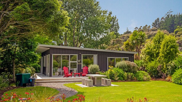 A modern house with a patio, red chairs, and a garden.