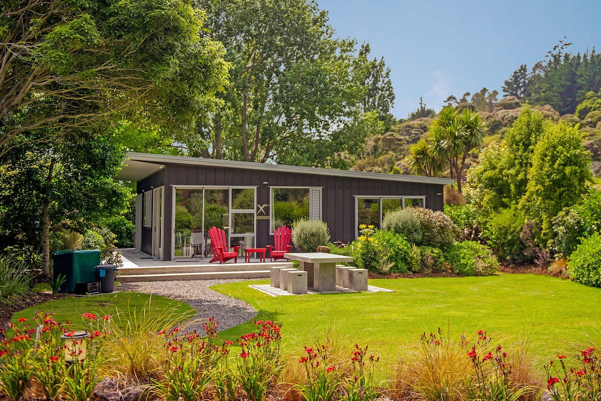 A modern house with a patio, red chairs, and a garden.