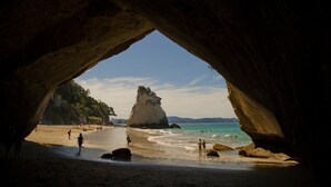 A beach scene framed by a large rock arch with people on the sand and water.