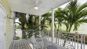 A wooden deck with white railings, a ceiling fan, and a table and chair.