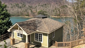 A house with a stone foundation, a sloped roof, and a view of a lake and mountains.