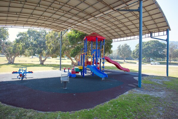 A playground with a covered play area, including a slide and climbing structures. - Hat Head Holiday Park (Hat Head)