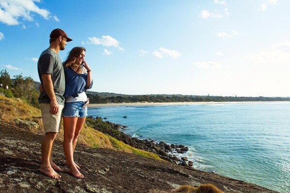 Um casal parado em uma costa rochosa, com vista para uma praia e o oceano.