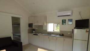 A compact kitchen with white cabinets, a microwave, a sink, and a refrigerator. There is a window providing natural light, and a television is mounted above the refrigerator.