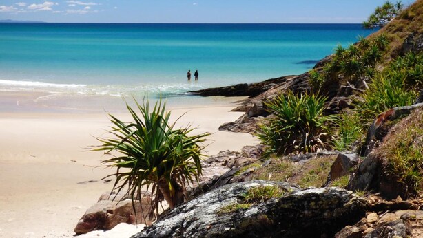 A beach with clear turquoise water, rocky outcrops, and green vegetation.