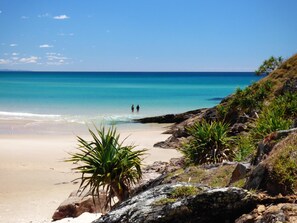 Una playa con aguas turquesas cristalinas, afloramientos rocosos y vegetación verde.