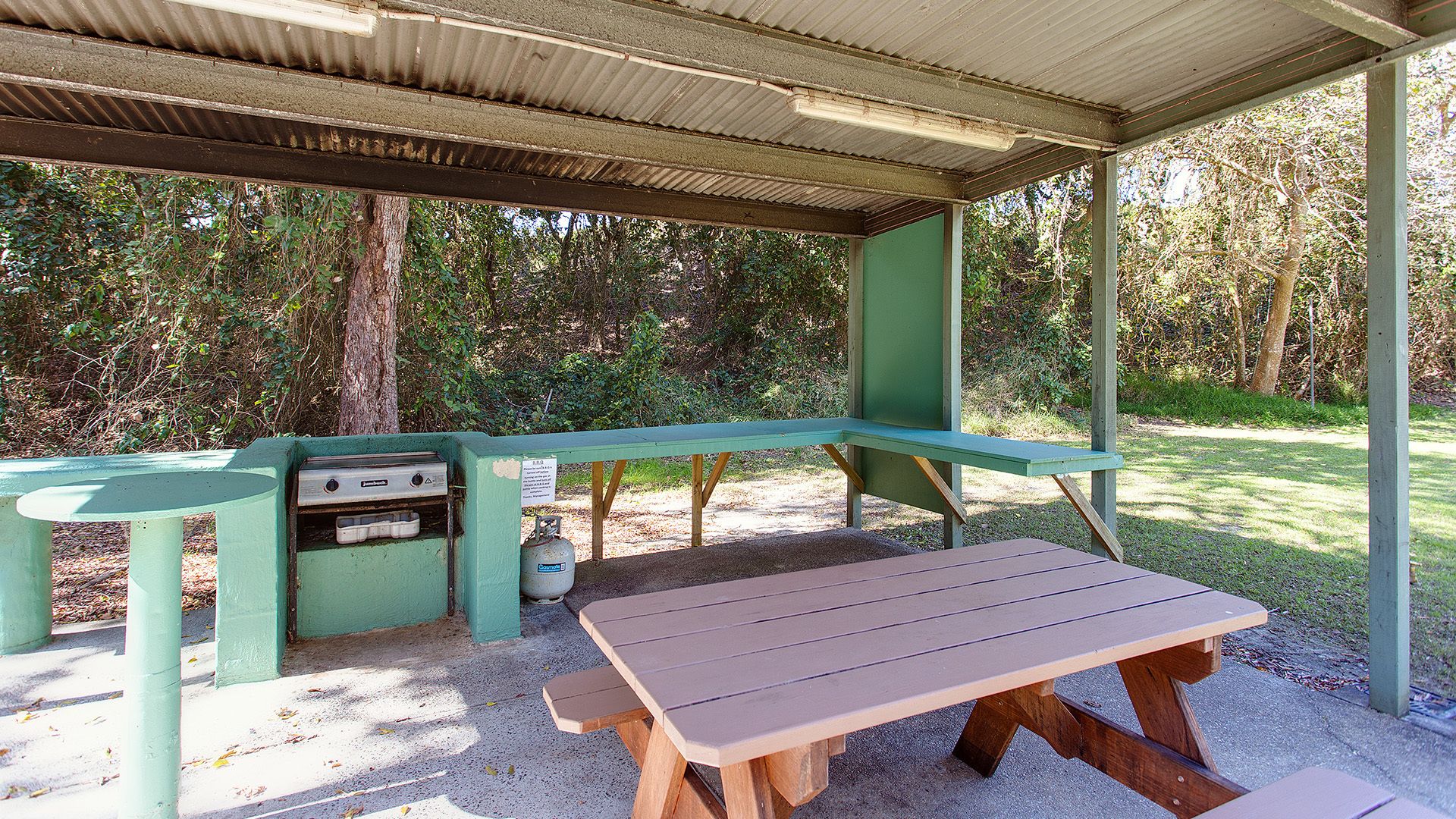 A picnic area with a table and grill, surrounded by trees.