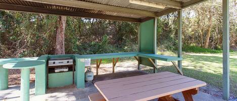 A picnic area with a table and grill, surrounded by trees.