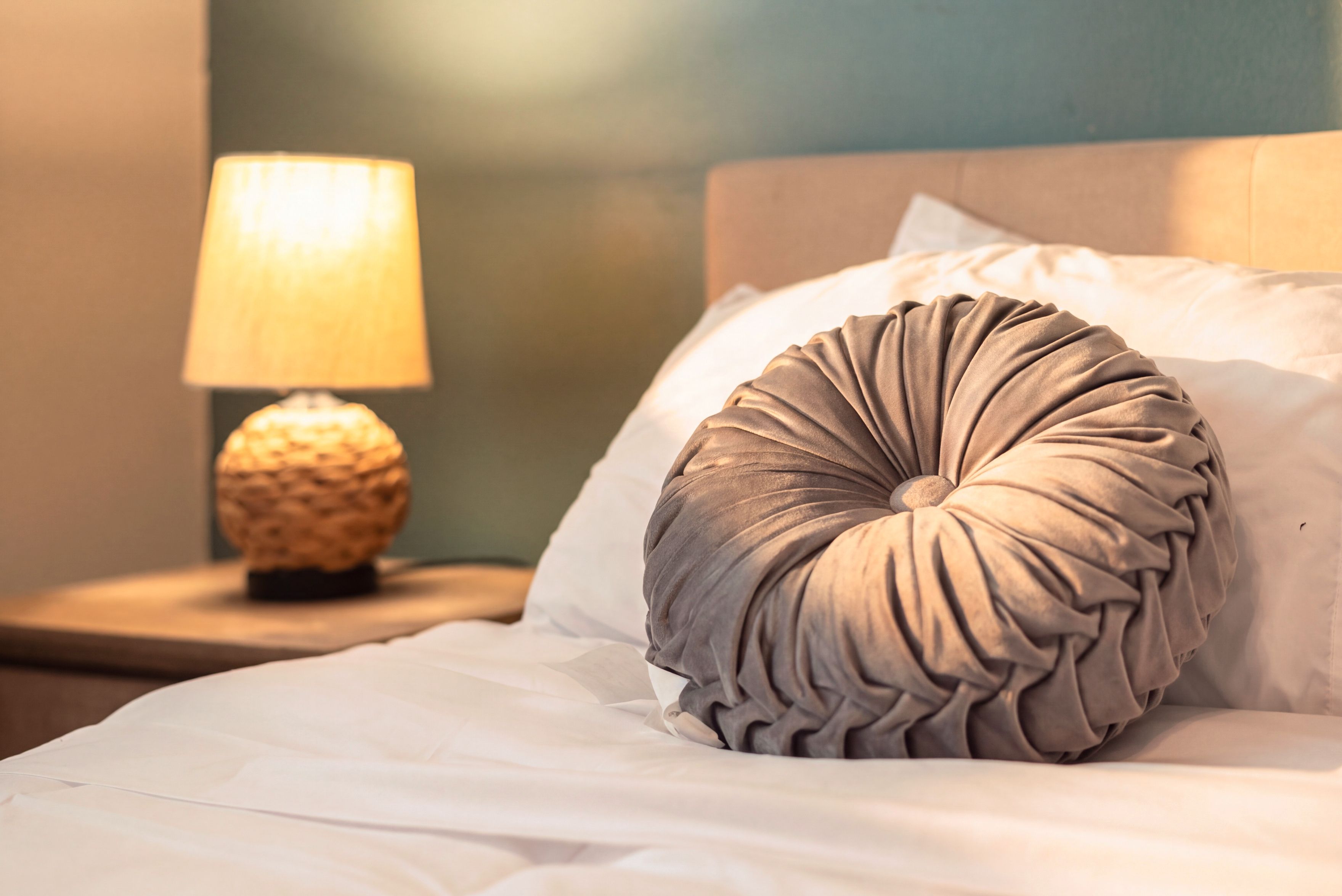 A bed with a textured pillow and a lamp on a bedside table.