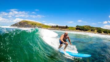 A man surfing on a clear day with a view of a beach and a hill in the background.