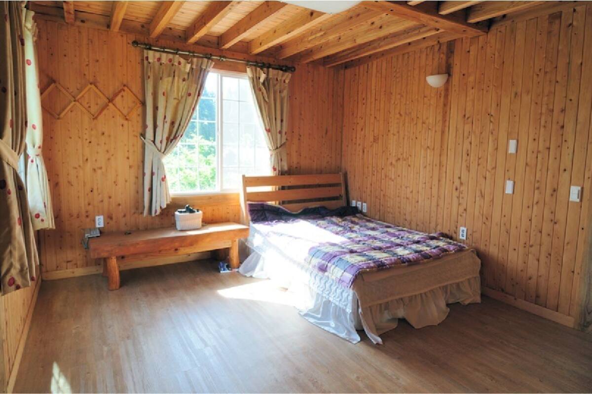 Une chambre dans une cabane en bois, avec un lit, un banc et une fenêtre.