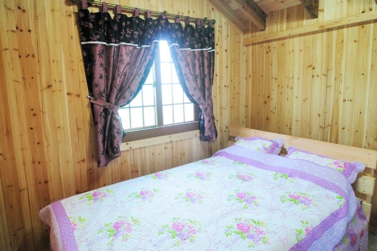 Une pièce en bois avec un lit, une literie à motifs floraux et une fenêtre avec des rideaux.