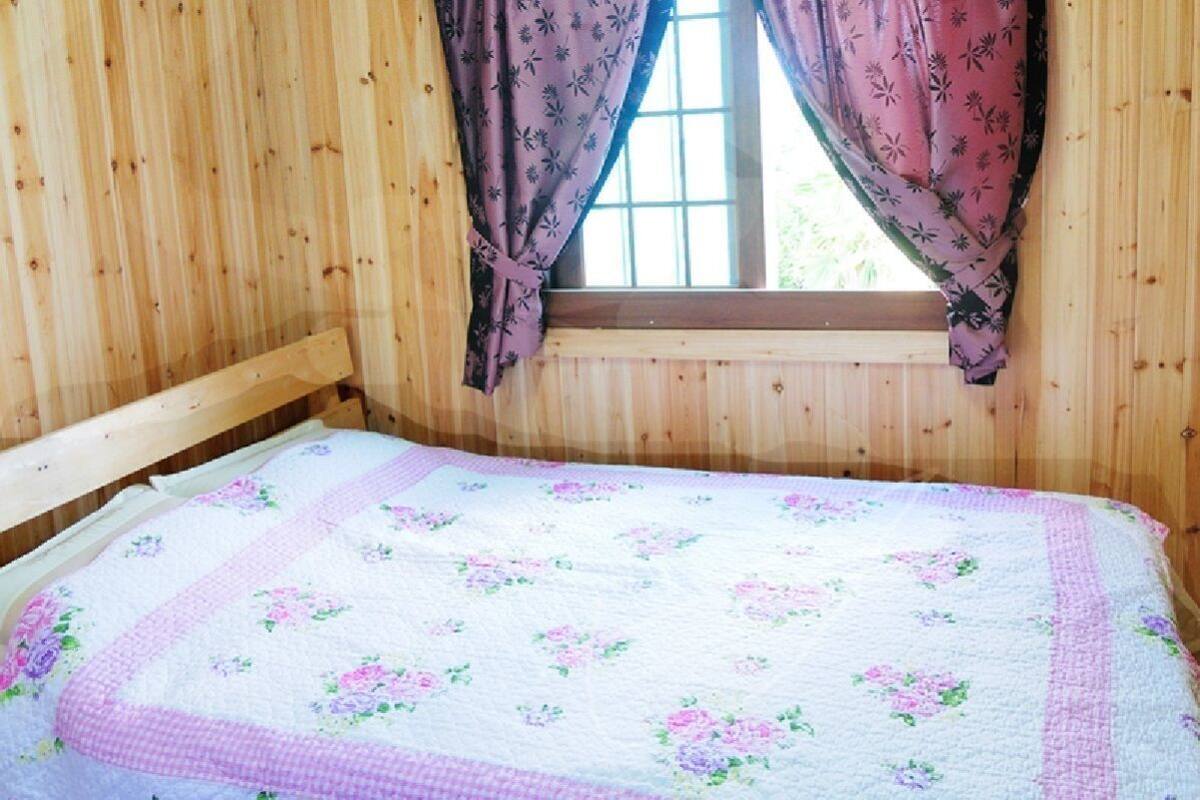 Une pièce de cabane en bois comprenant un lit, des rideaux à motifs floraux et une fenêtre.