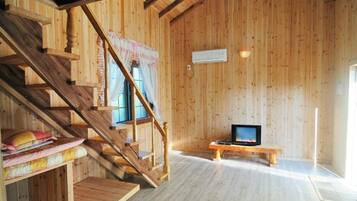 A wooden interior with a staircase, a television on a bench, and a window with curtains.