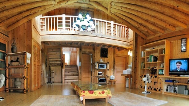 Un intérieur spacieux en bois, avec un plafond haut, un balcon, une table à manger et un téléviseur.