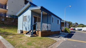 A small, single-story house with a porch and a wooden deck. - Horseshoe Bay Holiday Park (South West Rocks)