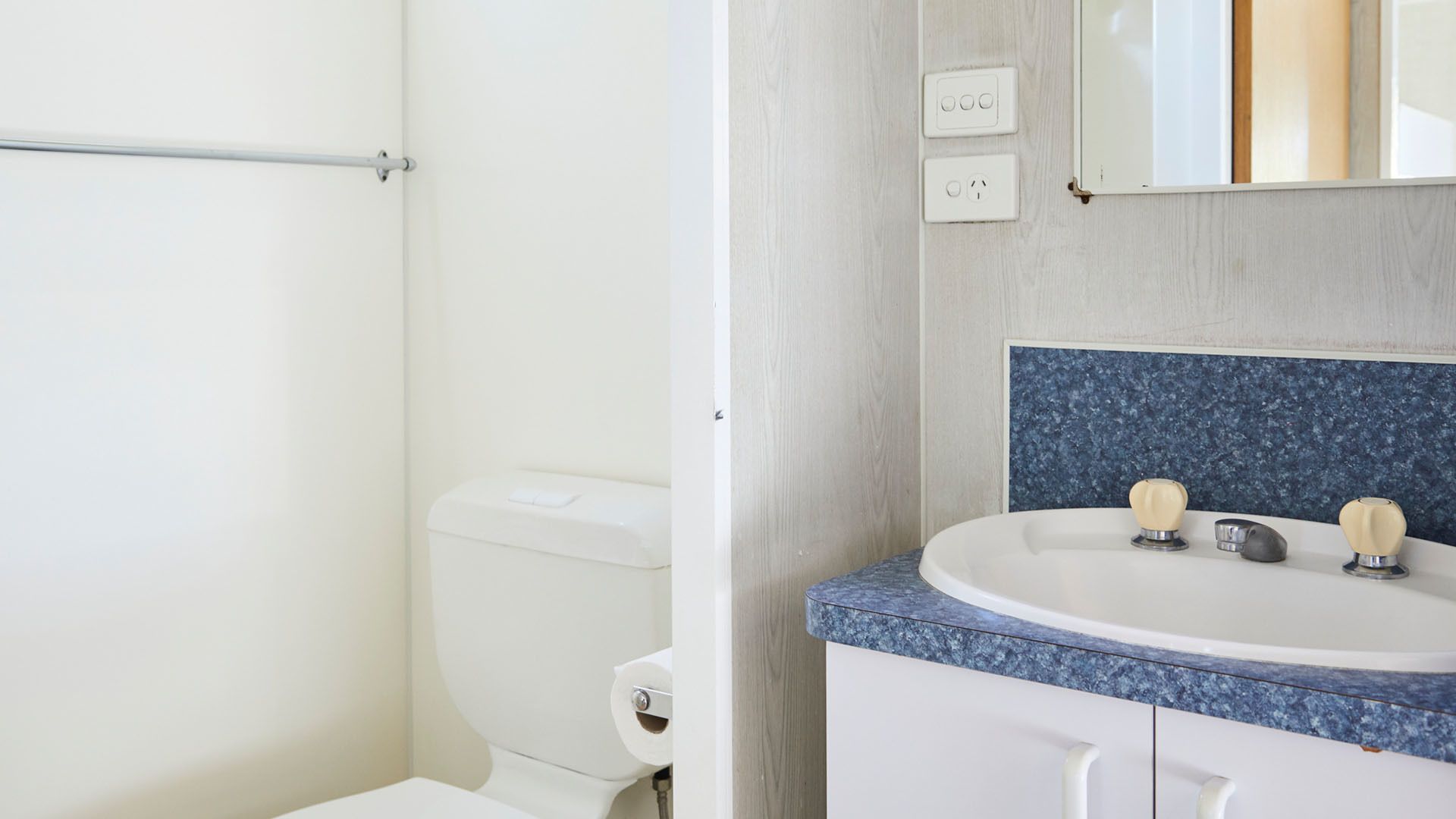 A bathroom with a toilet, a sink with a blue countertop, and a mirror above the sink.