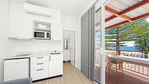 A modern kitchen with white cabinets, a microwave, and a refrigerator. There is a sliding glass door leading to an outdoor deck with a table and chairs. - Horseshoe Bay Holiday Park (South West Rocks)
