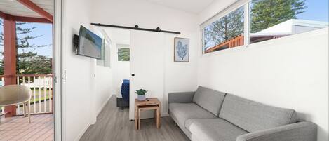 Ett modernt vardagsrum med en grå soffa, ett litet träbord med en växt och en tv som är monterad på väggen.