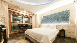 A modern hotel room with a large bed, a small desk, a chair, and a window with a geometric pattern. - Hotel Tops Ville (Gangneung)