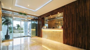 A hotel reception area with a wooden reception desk, a glass entrance, and a potted plant. - Hotel Tops Ville (Gangneung)