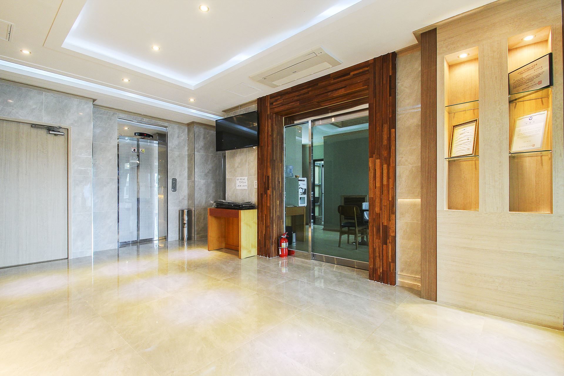A modern hotel lobby with a marble floor, a reception desk, and a glass door leading to a dining area.
