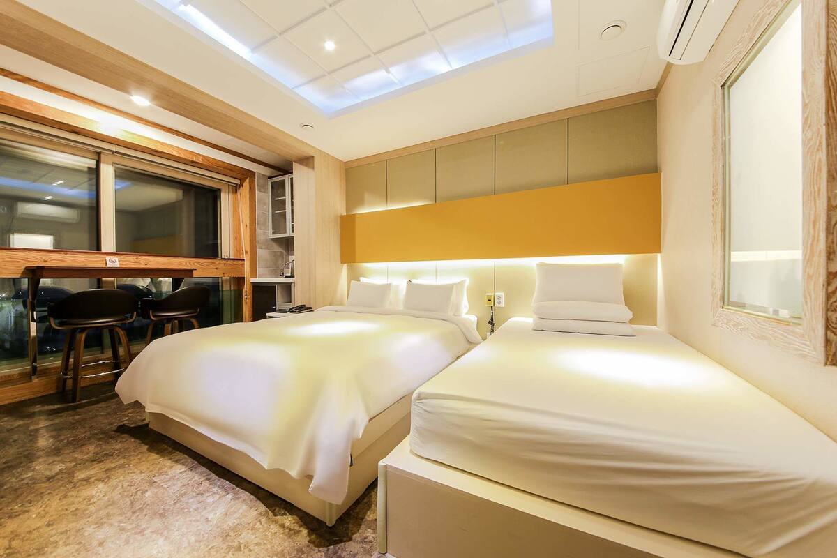 A hotel room with two beds, a desk, and a window.