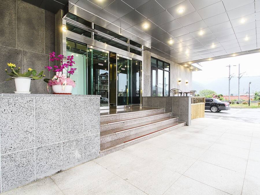 A modern building entrance with a stone facade, glass doors, and steps leading to a covered area.