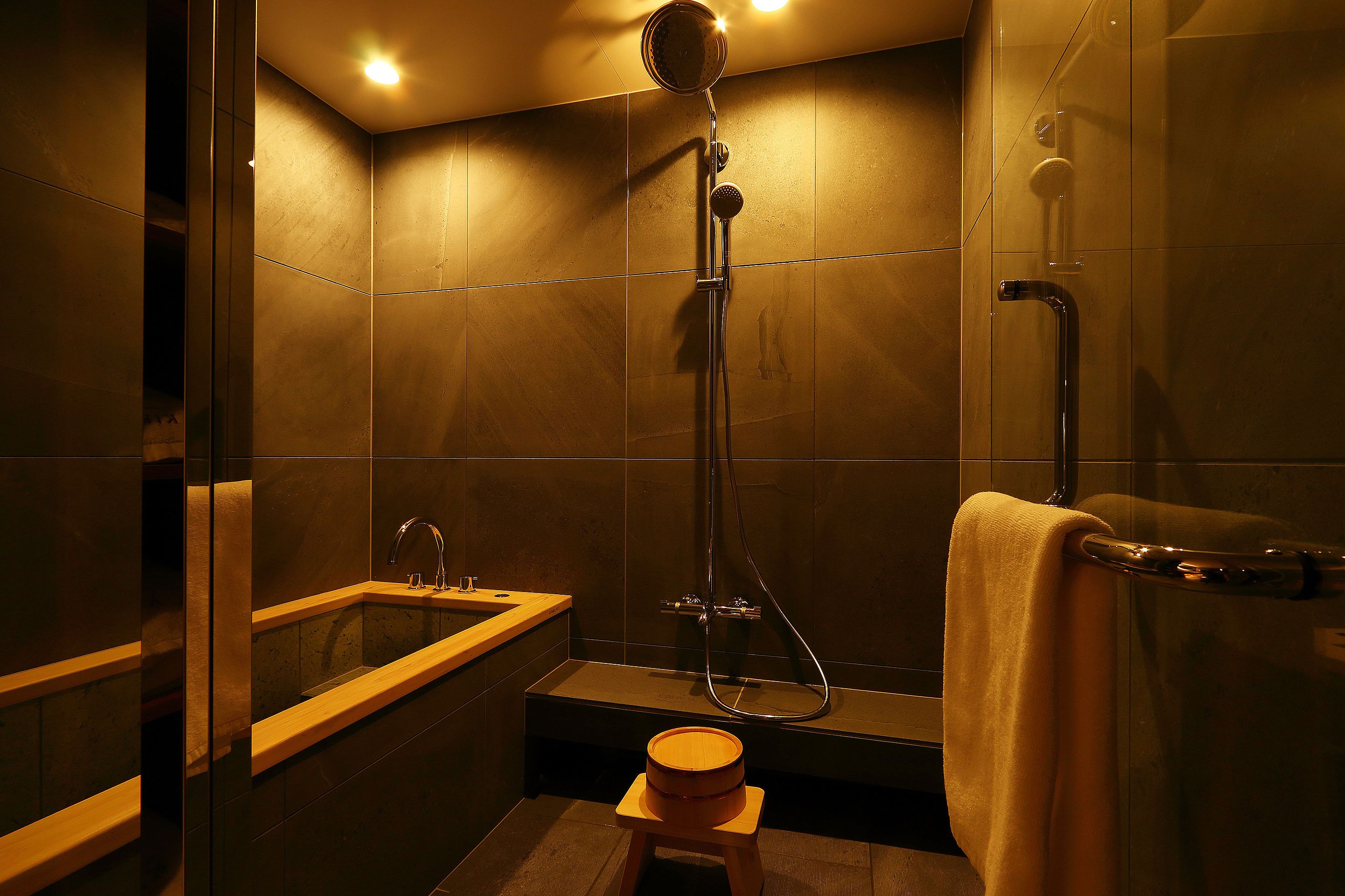 A modern bathroom with a bathtub, shower, and a wooden stool.