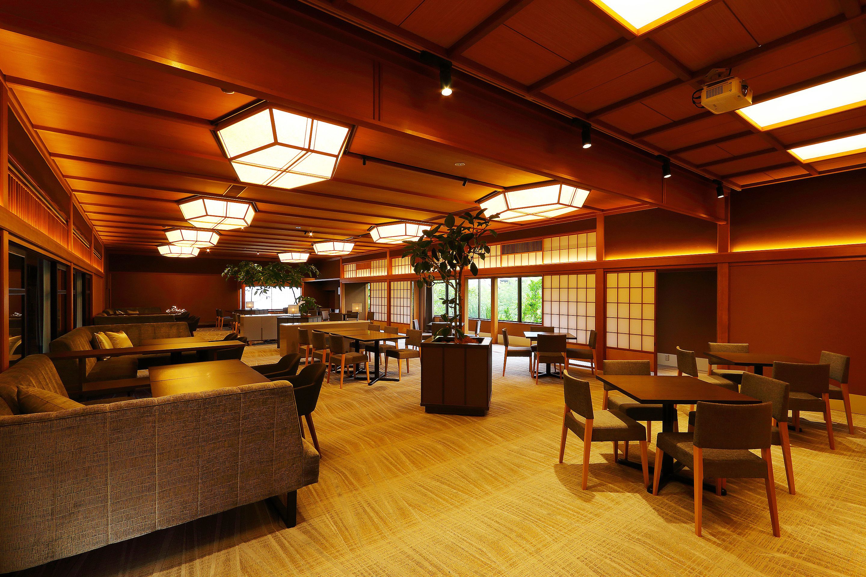 A spacious room with multiple seating areas, including sofas and tables, and large windows allowing natural light.