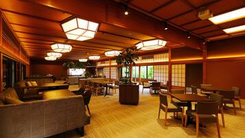 A spacious room with multiple seating areas, including sofas and tables, and large windows allowing natural light.