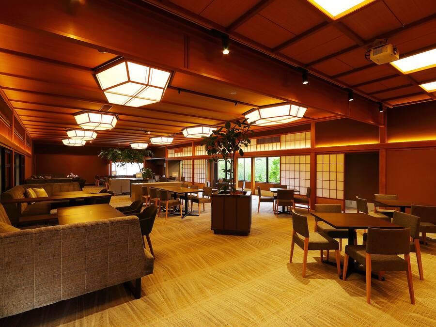 A spacious room with multiple seating areas, including sofas and tables, and large windows allowing natural light.