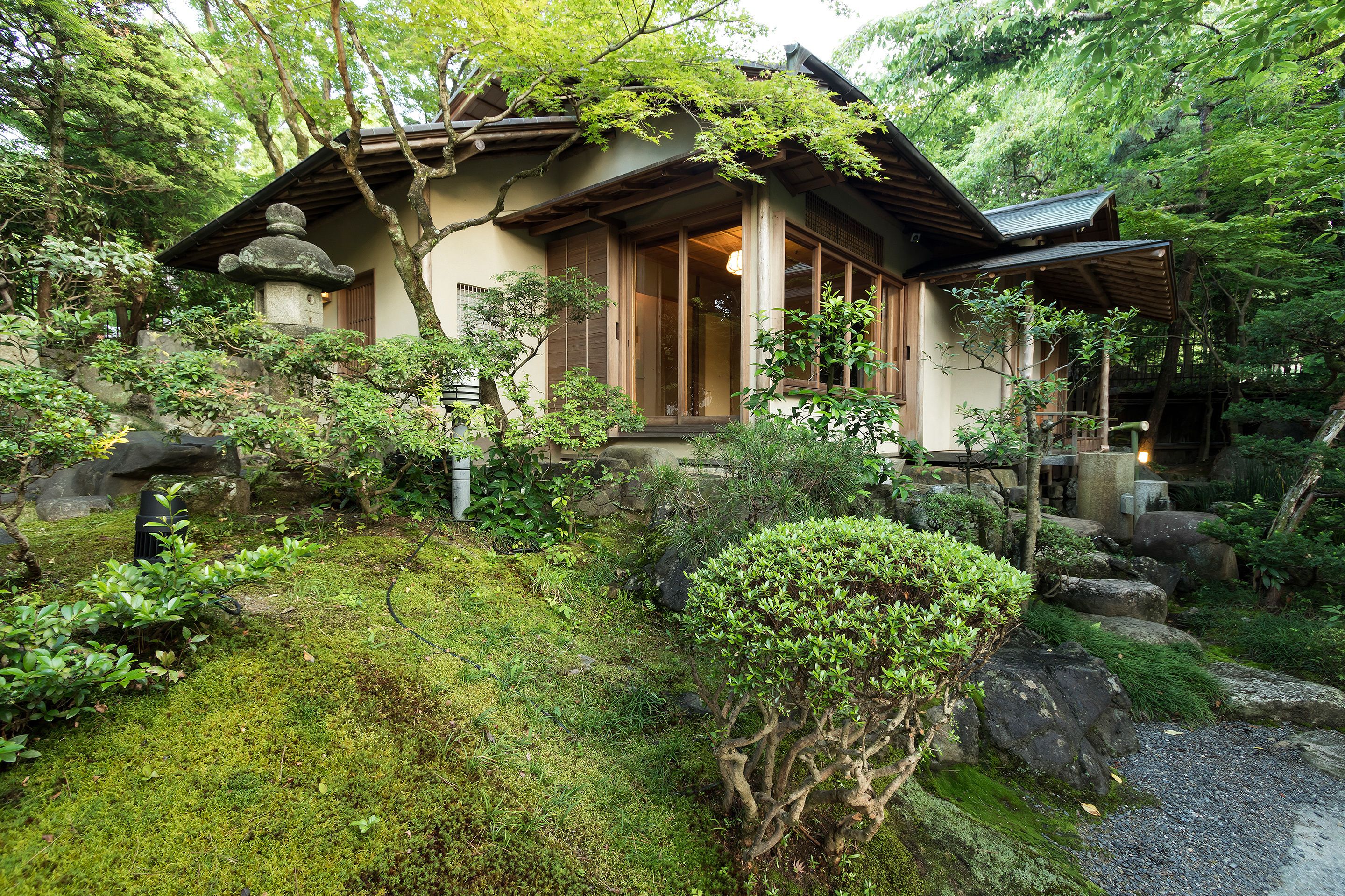 A traditional Japanese house surrounded by lush greenery and rocks.