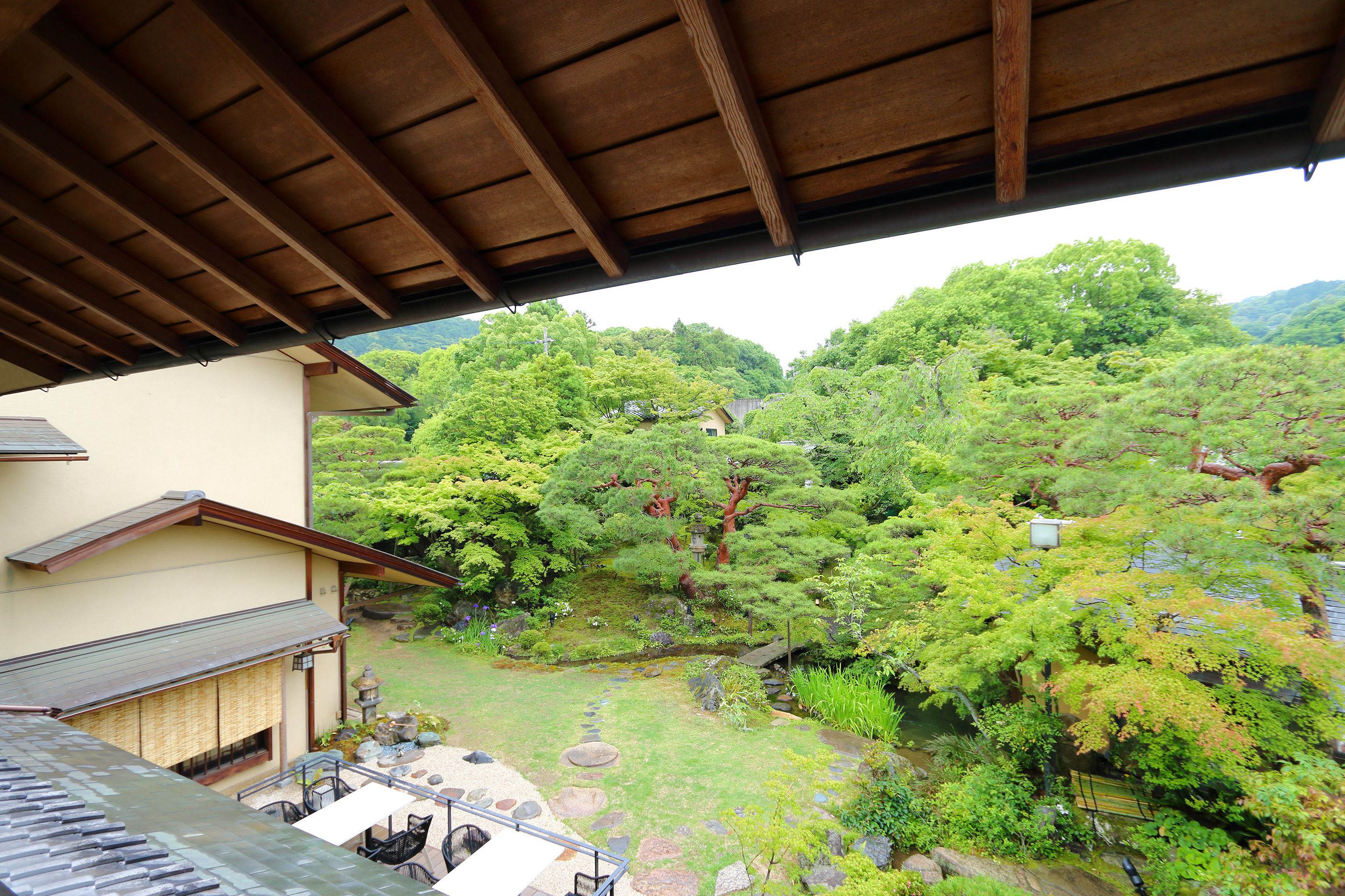 Un edificio tradicional japonés con tejado de madera y vistas a un exuberante jardín con varios árboles y un pequeño estanque.