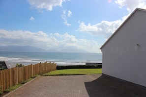 A paved pathway leading to a white building with a view of the sea and mountains in the distance. - Luxury Beach View Cottage (Inch)