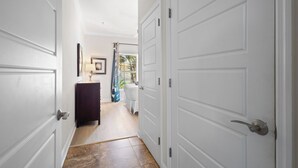 A hallway with white doors, a dark-colored dresser, and a bed with a blue curtain. - Dream Sunsets & Coastal Bliss–Beach Club 108A / RVA (Sarasota)
