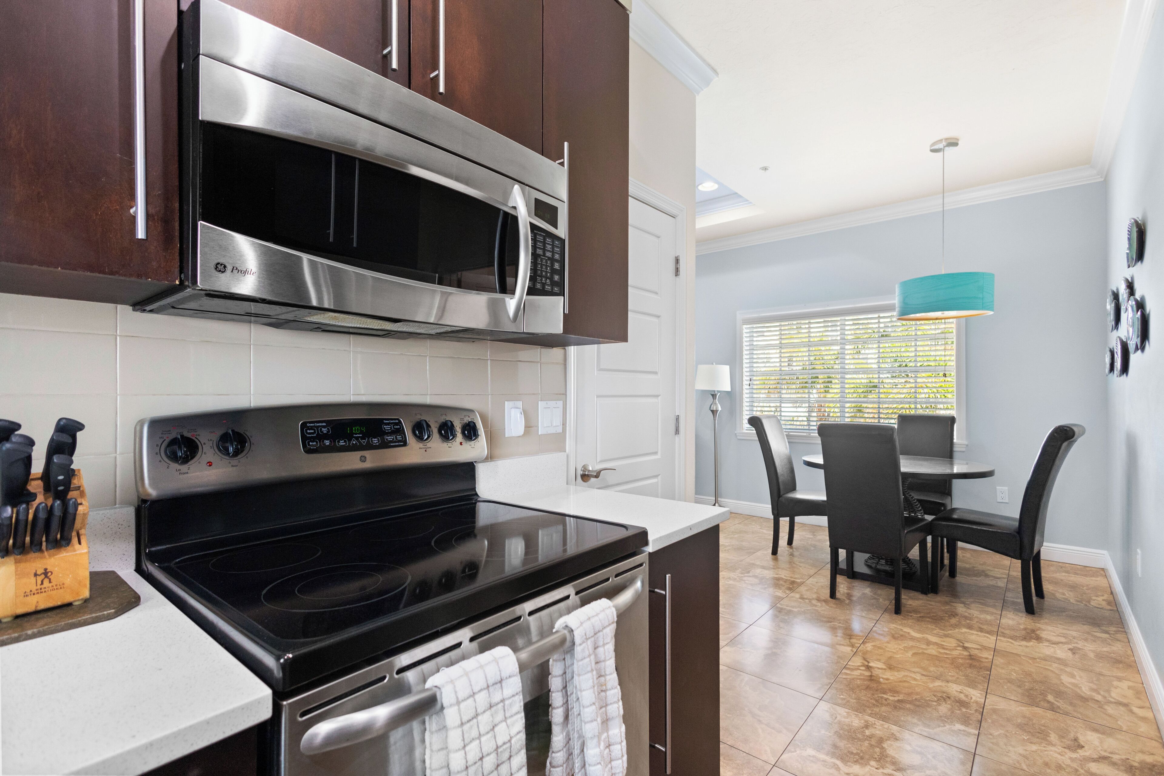 A modern kitchen with stainless steel appliances, a dining area with a table and chairs, and a window with blinds.