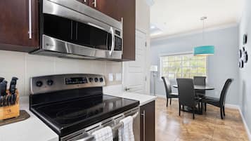 A modern kitchen with stainless steel appliances, a dining area with a table and chairs, and a window with blinds.