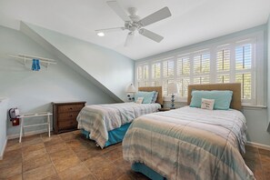 A bedroom with two beds, a ceiling fan, and a window with shutters.