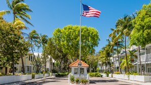 Un hôtel situé sur la côte, avec un mât de drapeau, une enseigne d’accueil et une clôture blanche en bois.