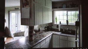 A kitchen with white cabinets, a granite countertop, and a window with a view of greenery outside. - Charming cottage minutes from Gaelic College and Baddeck with WIFI (Baddeck)