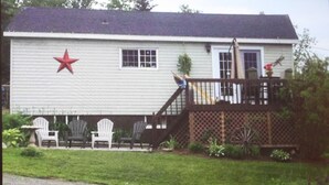 A house with a red star on the side, a porch with chairs, and a wooden fence. - Charming cottage minutes from Gaelic College and Baddeck with WIFI (Baddeck)