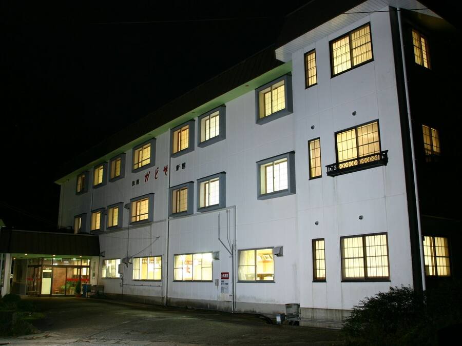 En byggnad med flera våningar, upplysta fönster och en skylt med text på ett främmande språk.