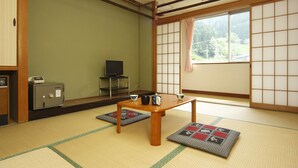 A traditional Japanese room with tatami flooring, a low wooden table, a safe, and a television.