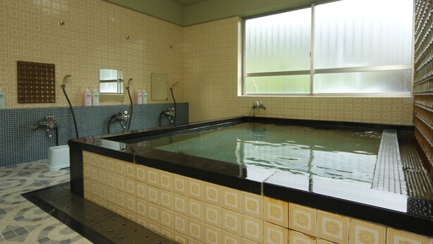 A large bathtub with a tiled surround, a window with blinds, and a tiled wall with a geometric pattern.