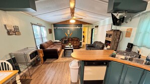 Een compacte leefruimte met een kitchenette, een eethoek en een zithoek met een bank en stoelen.
