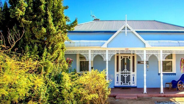 Een tweelaags huis met een blauwe gevel en witte details, voorzien van een veranda met decoratieve spijlen en een kleine terrasstoel.