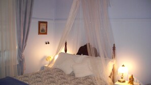 Een bed met hemelbed, een nachtkastje met een lamp en een schilderij aan de muur.