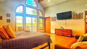A bedroom with a large bed, a television, a dresser, and a window with a view. - Lakefront, Hot Tub, Game Room, Canoe, Kayaks, Decks, Firepit (Tobyhanna)